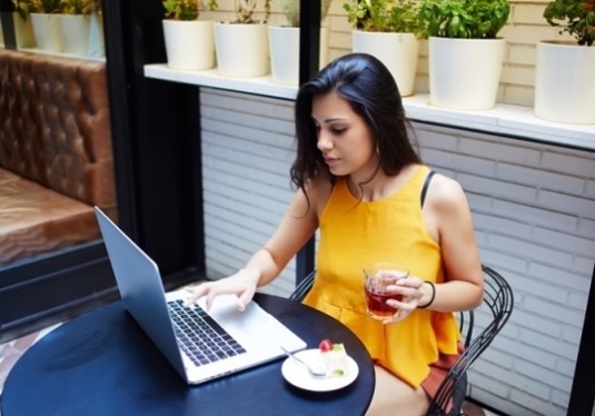 Woman drinking tea sitting at a table working on a laptop
