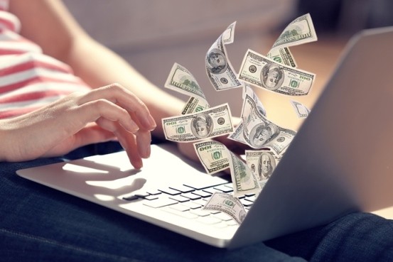 Woman sitting on the floor using laptop with money floating in front of screen