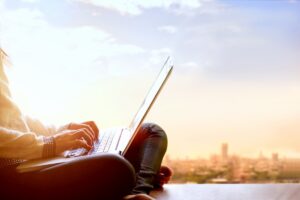Woman using laptop computer and sitting on the view of a skyscraper with cityscape